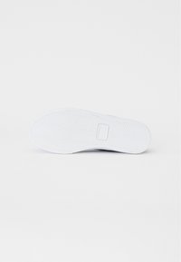 Suela de zapatilla blanca con un patrón de espiga, textura plana y suave, que presenta un parche de marca rectangular cerca del talón.