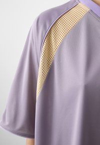 Top in jersey color lavanda con pannello in rete di tonalità più chiara, che mostra una vestibilità morbida e un design moderno.