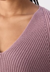 Maglione lilla lavorato a maglia con scollatura a V. Presenta un motivo a coste textured. Il tessuto sembra leggero e traspirante.