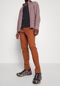 Rutig röd och vit skjorta, svart linne, bruna tajta byxor och svarta träningsskor med orange detaljer och nitar.