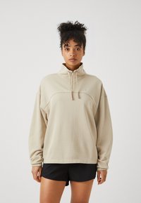 Felpa beige con collo alto, zip a un quarto e polsini a coste. Presenta cuciture tono su tono e un piccolo logo sul petto.