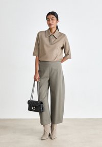 Beżowa koszula z krótkim rękawem i kołnierzykiem, ozdobiona ćwiekami, zestawiona z szerokimi oliwkowymi spodniami i czarną torebką z ćwiekami. Beżowe botki za kostkę.