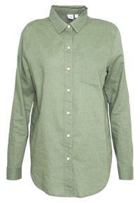 Chemise à manches longues verte avec un col à boutons, une poche avant, et cinq boutons blancs le long du centre. Fabriquée en tissu texturé.
