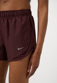 Burgunderfarbene Nike Sportshorts mit elastischem Bund, seitlichen Netzpaneelen und einem dezenten silbernen Logo auf dem linken Bein.
