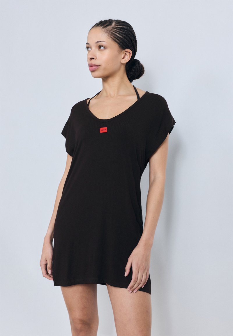 Vestido túnica curto de manga curta preto com decote em V e um pequeno emblema vermelho. Confeccionado em material leve, apresenta um corte descontraído e fendas laterais.