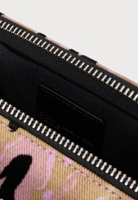 Közeli kép egy rózsaszín és bézs színű szövetzsákról, fekete belsővel és részben nyitott ezüst színű fém cipzárral.