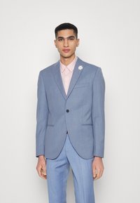 Blazer azul claro com um corte ajustado, fecho de um único botão e lapelas em pico, combinado com uma camisa rosa pastel e detalhe de alfinete floral.