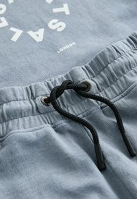 Ceinture en tissu gris avec cordon noir noué, fronces élastiques et texte blanc « SALE » et « LONDON » partiellement visible en haut.