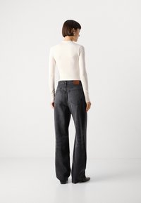 Zwarte wijde jeans met hoge taille, gedetailleerde stiksels en een leren patch op de achterkant. G gedragen met een aansluitende crèmekleurige top met lange mouwen.