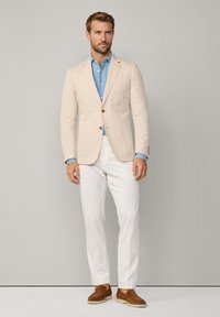 Blazer beige ajusté, chemise bleu clair, pantalon blanc et chaussures dSlip-on marron. Tissu lisse avec des lignes épurées et un minimum de détails.