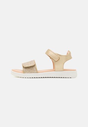 Sandalias doradas con una correa brillante, cierre de velcro ajustable, acentos beige y una suela blanca texturizada. Diseño ligero y abierto.