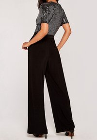 Pantalons larges noirs associés à un haut argenté à manches courtes en métal avec un motif texturé. Tissu lisse et taille ajustée.