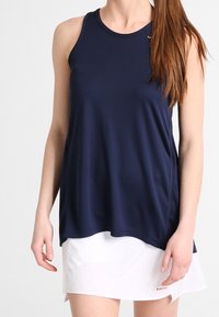 Mörkblå atletisk linne med rund halsringning och en lös passform, tillverkat av ett glatt tyg. Kombineras med en vit tenniskjol.