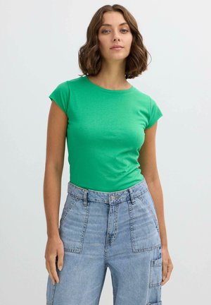 Camiseta verde de manga corta hecha de tejido ligero, con cuello redondo y forma ajustada, combinada con unos vaqueros de tiro alto de color azul claro.
