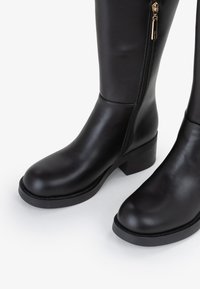 Stivali neri alti fino al ginocchio realizzati in pelle liscia, dotati di cerniera laterale e tacco basso a blocco, con punta rotonda e design pulito.