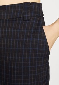 Svart rutiga byxor med ett hundtandsmönster och blå linjer, en slät tygtextur och en sidficka. Midjan har en bältesöglor.