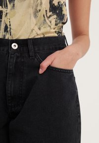 Černé džínové kalhoty s vysokým pasem, vybavené kovovým zapínáním na knoflík, bočními kapsami a viditelnými švy pro zvýšení odolnosti.