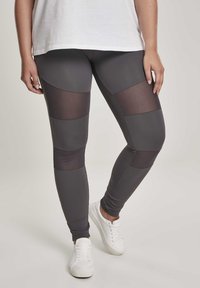 Graue Sportleggings mit Mesh-Einsätzen an den Oberschenkeln, glatter Textur und tailliertem Design. Kombiniert mit weißen Sneakers.