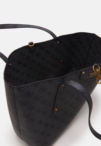 Stor sort tote taske med en tekstureret overflade, guldfarvede hardware-detaljer og et mønstret interiør. Åben top med to skulderremme.