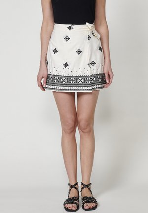 Witte rok met zwarte geborduurde geometrische patronen aan de zoom en taille. Voorzien van een zijstrik en een uitlopende stijl. Textiel met een zachte afwerking.