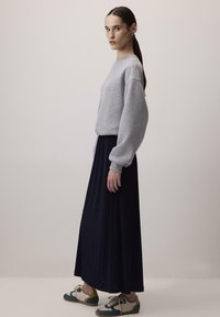 Felpa grigia oversize, gonna maxi blu scuro e sneakers multicolori. Tessuto morbido, vestibilità comoda, maniche lunghe e silhouette elegante.