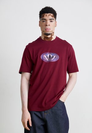 T-shirt in cotone bordeaux con scollatura rotonda e maniche corte, caratterizzato da un logo Adidas circolare blu e bianco al centro.