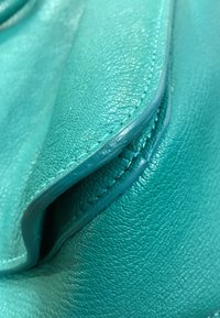 Gros plan sur un cuir texturé turquoise avec des coutures détaillées le long des bords repliés d'un article en cuir.