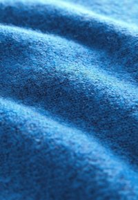 Gros plan d'un tissu en laine bleu montrant une texture douce et duveteuse ainsi que des plis légers sous la lumière naturelle.