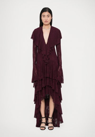 Abito in pizzo color bordeaux con strati arricciati, scollo a V profondo e maniche a campana. Presenta un orlo asimmetrico, abbinato a sandali neri con cinturini.