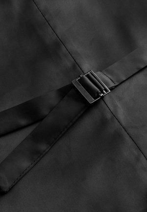 Tessuto nero con una superficie liscia, caratterizzato da una larga fascia al centro fissata da una fibbia quadrata in metallo nero.