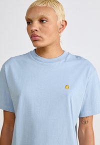 Lichtblauw katoenen t-shirt met een ronde hals en korte mouwen. Heeft een klein gele logo op de borst. Soepele textuur en relaxed fit.