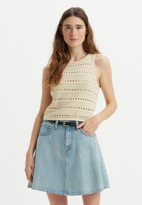 Top in maglia crema con motivo a traforo, abbinato a una mini gonna in denim azzurro chiaro dal taglio svasato e una cintura nera.