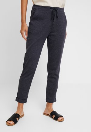 Pantalons à carreaux bleu marine avec taille élastique et cordon de serrage. Manches retroussées et poches latérales. Associés à des sandales à glissière noires.