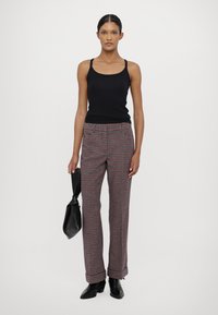 Svart tanktopp, rutete bukser i rødt, svart og hvitt, rett snitt, med en svart veske. Glatt stoff, elastisk midjebånd, minimalistisk design.