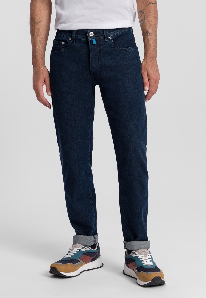 Donkerblauwe denim jeans met een slim fit, voorzien van een knoopsluiting, vijf zakken en opgerolde manchetten, gecombineerd met multicolore sneakers.