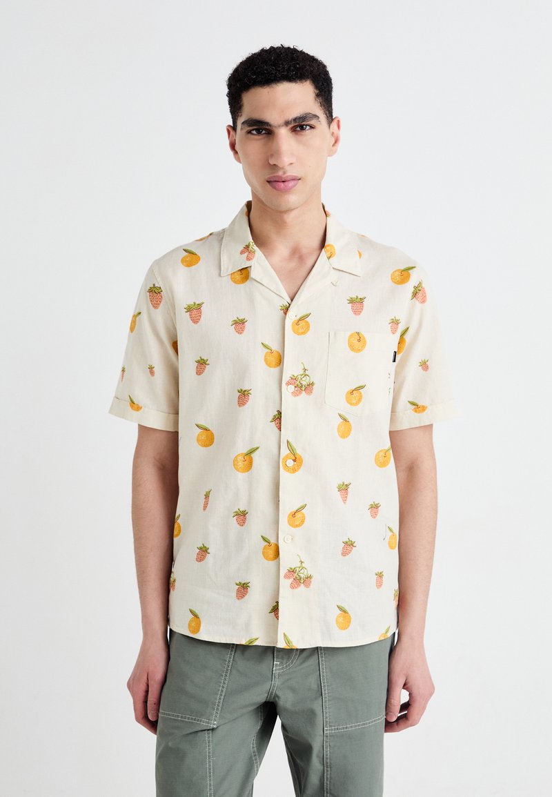 Camisa de manga corta en tejido de color beige claro con un estampado de frutas de naranjas y fresas. Bolsillo frontal y cuello abotonado.