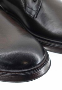 Scarpe in pelle nera con una finitura lucida, punte arrotondate e suola cucita. Il design presenta lacci e una texture liscia e morbida.