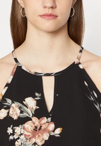 Top preto floral com design halter, apresentando um decote em formato de buraco-chave. Acentuado com padrões florais multicoloridos no tecido.