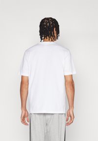 Λευκό βαμβακερό T-shirt με στρογγυλή λαιμόκοψη και κοντά μανίκια, με χαλαρή εφαρμογή και λεία υφή. Εμφανίζεται η πίσω όψη.