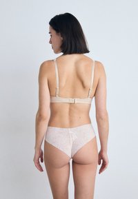 Sutien bej cu bretele ajustabile, având o închidere cu cârlig și ochi. Asortat cu lenjerie intimă roz deschis, cu un model din dantelă florală.