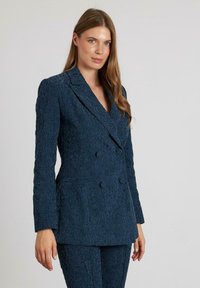 Blazer azul marino de doble botonadura con un patrón floral texturizado. Presenta un corte entallado, solapas de muesca y dos bolsillos frontales.