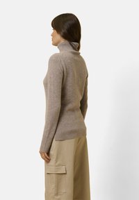 Hellbrauner Rollkragenpullover aus weichem Material, taillierte Silhouette, gerippte Bündchen und Saum, getragen mit einem beigen Cargo-Rock.