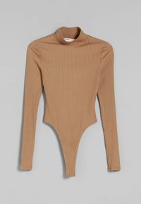 Räfflad långärmad beige bodysuit med hög hals och tryckknappsstängning vid gren, utlagd platt på en grå bakgrund.