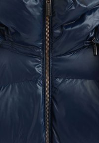 Veste rembourrée bleu marine avec une fermeture éclair centrale à l'avant, texture lisse et brillante, et fermeture éclair métallique contrastante avec tirette.
