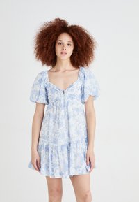 Vestido floral azul com mangas bufantes, decote em V e detalhe em fenda. Apresenta uma bainha em camadas com babados e textura de tecido leve.