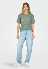 Top corto de punto abierto en verde claro, con un dobladillo ondulado, combinado con jeans de tiro alto, de ajuste holgado, en azul claro y zapatillas blancas.