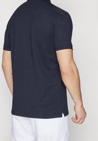 Marinblå polo t-shirt med en slät yta, korta ärmar och klassisk krage. Har sidslitsar vid fållen för komfort.