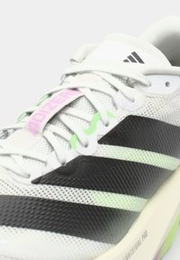 Running shoes with a breathable mesh upper in white, black accents, and green and pink details. Features a textured sole for traction.