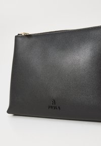 Pochette en cuir noir avec une texture lisse, fermeture éclair et logo "FURLA" embossé à l'avant. Design rectangulaire compact.
