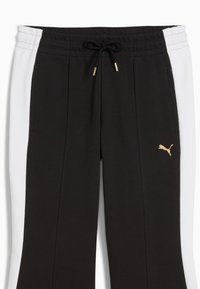 Pantalones deportivos negros y blancos con cintura ajustable mediante cordón, detalles en dorado y un pequeño logo dorado en la pierna izquierda. Tejido texturizado.
